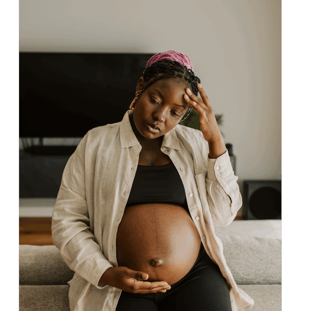 Femme enceinte assise, touchant son ventre et son front – Inconforts liés à la grossesse et accompagnement ostéopathique à Montréal